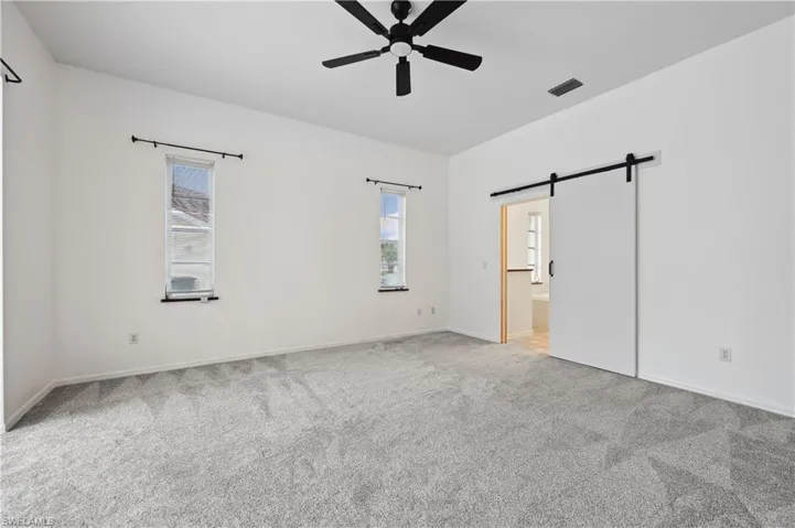 Unfurnished bedroom featuring a barn door, light colored carpet, connected bathroom, and a ceiling fan
