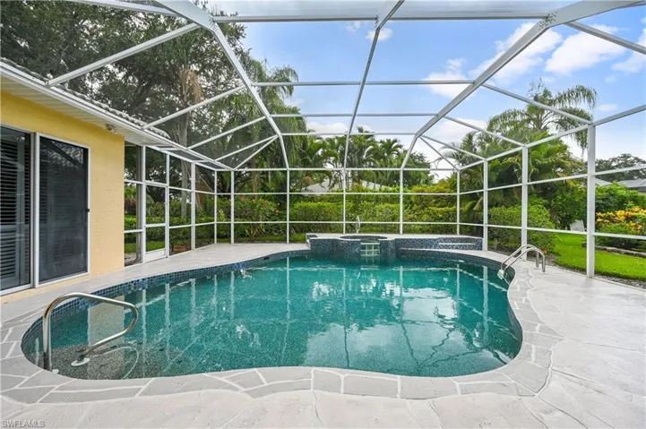 View of swimming pool featuring a sunroom, glass enclosure, a patio, and a pool with connected hot tub