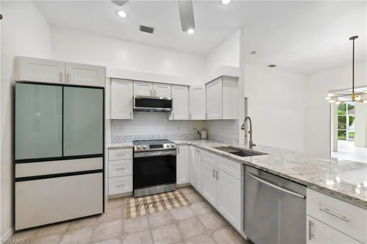 Kitchen featuring backsplash, stainless steel appliances, light stone counters, pendant lighting, and white cabinets