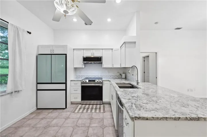 Kitchen with light stone counters, stainless steel appliances, backsplash, white cabinetry, and a peninsula