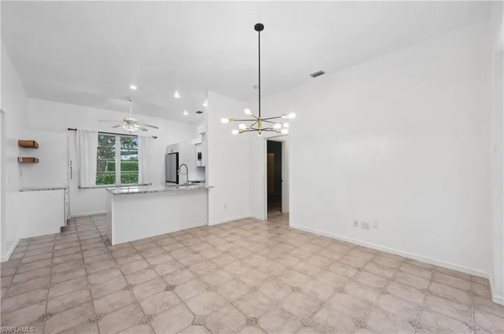 Kitchen featuring a ceiling fan, white cabinets, a peninsula, light stone counters, and a chandelier