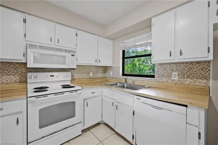 Kitchen with white appliances, light countertops, light tile patterned flooring, and white cabinetry