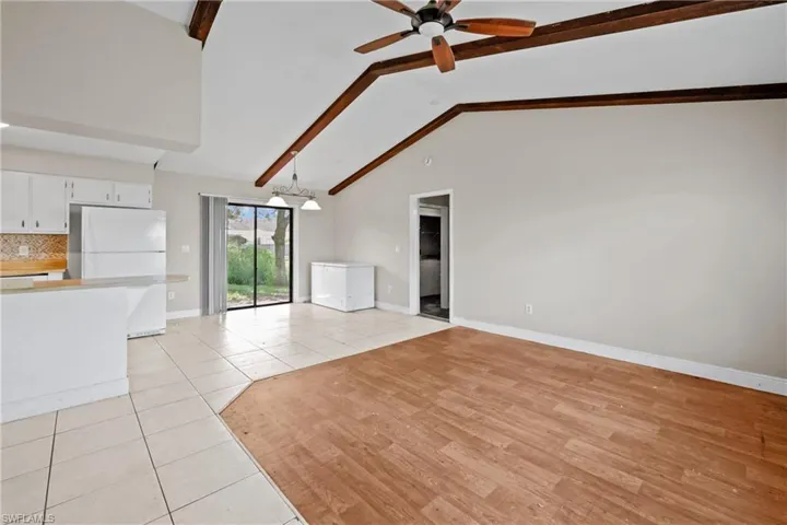 Unfurnished living room with ceiling fan, beam ceiling, light tile patterned floors, and high vaulted ceiling