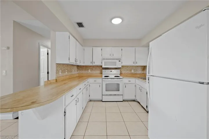 Kitchen with white appliances, a peninsula, tasteful backsplash, and light tile patterned floors