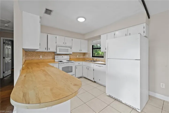 Kitchen featuring white appliances, light countertops, white cabinetry, and light tile patterned floors