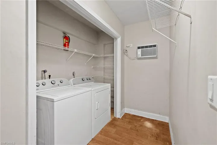Laundry area with washing machine and clothes dryer, light wood finished floors, and an AC wall unit