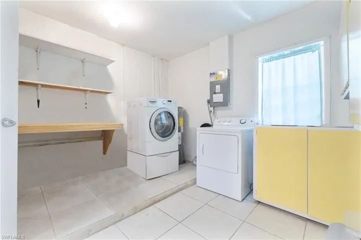 Laundry area with washing machine and clothes dryer, electric panel, and light tile patterned floors