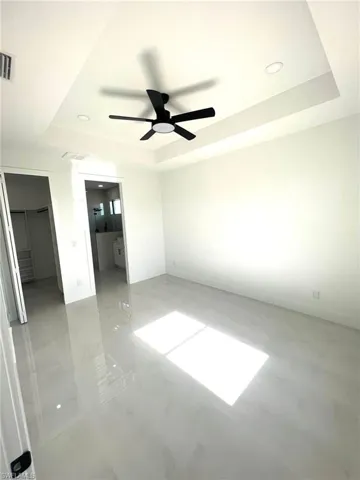 Tiled empty room featuring ceiling fan and a raised ceiling