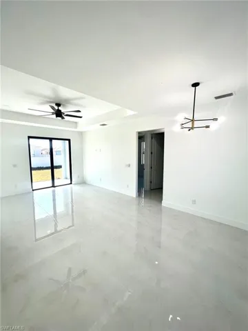 Tiled empty room featuring ceiling fan and a raised ceiling