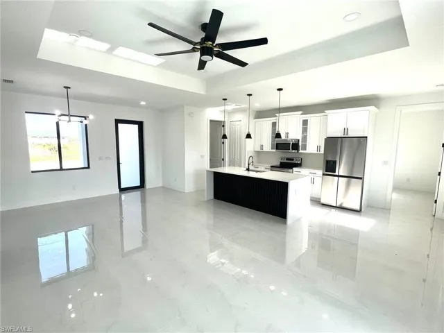 Kitchen featuring decorative light fixtures, light tile flooring, stainless steel appliances, a raised ceiling, and sink