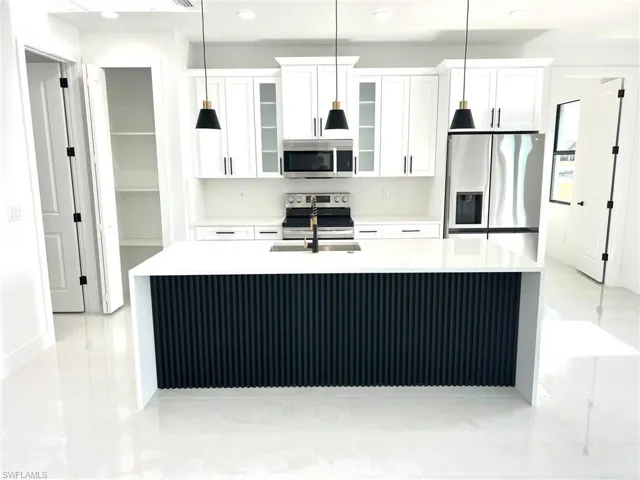 Kitchen with white cabinetry, stainless steel appliances, an island with sink, tasteful backsplash, and light tile floors