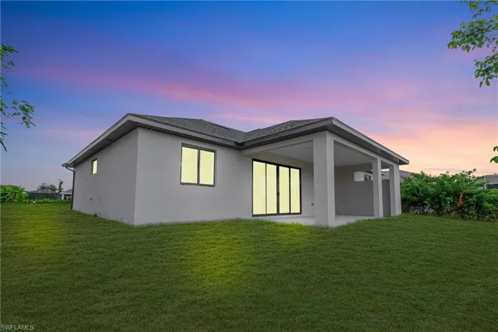 Back of house at dusk featuring a lawn, a patio area, and stucco siding