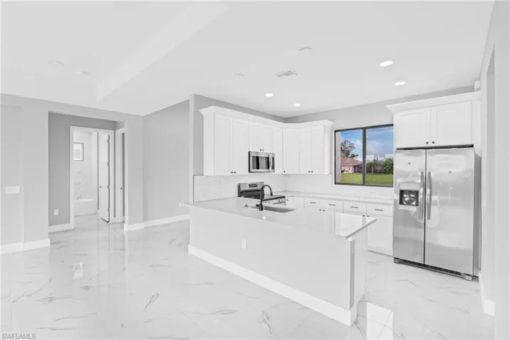 Kitchen with appliances with stainless steel finishes, light marble finish floors, white cabinets, light stone countertops, and recessed lighting