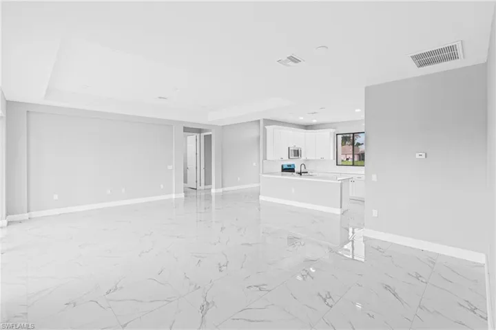 Unfurnished living room with light marble finish flooring, recessed lighting, and a tray ceiling