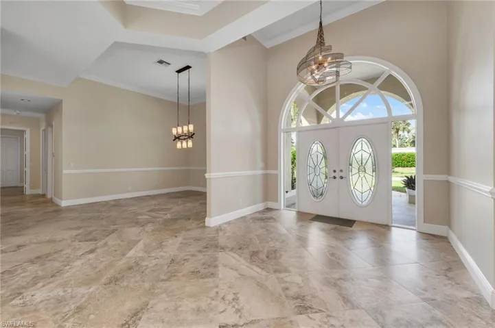 Entryway featuring french doors, a notable chandelier, ornamental molding, and a high ceiling