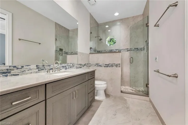 Guest suite/ Pool bath with toilet, walk in shower, vanity, and tile walls