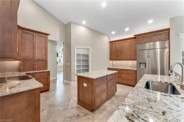 Kitchen with light stone counters, sink, tasteful backsplash, and built in fridge