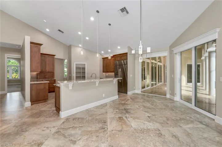 Kitchen featuring stainless steel built in refrigerator, pendant lighting, a breakfast bar, an island with sink, and high vaulted ceiling