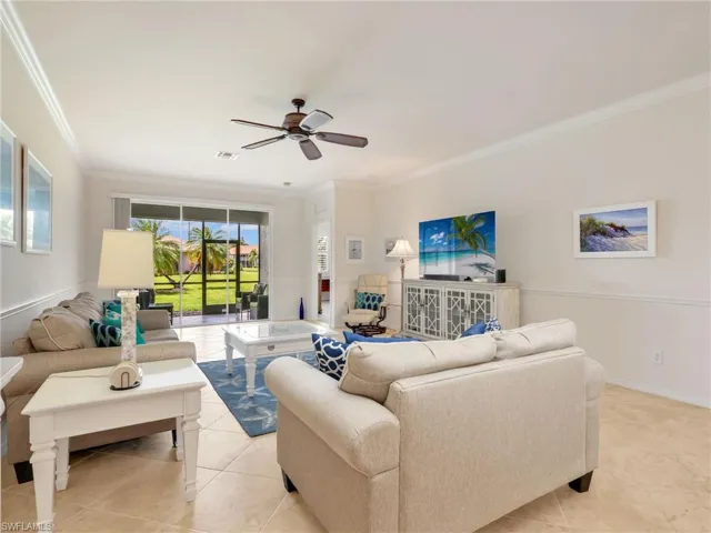 Living Room with Tile Flooring on the Diagonal, Crown Molding, Chair Rails, Ceiling Fan, & Sliders with Verticell Shades Leading to the Screened-In Lanai with Landscaped & Lake Views