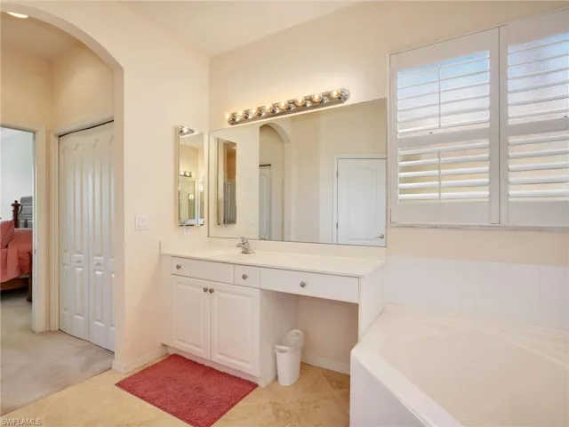 Primary En-Suite Bathroom with Curved Archway, Dual Vanities with Cultured Marble Countertops, Dual Medicine Cabinets, Tub, Linen Closet & Plantation Shutters
