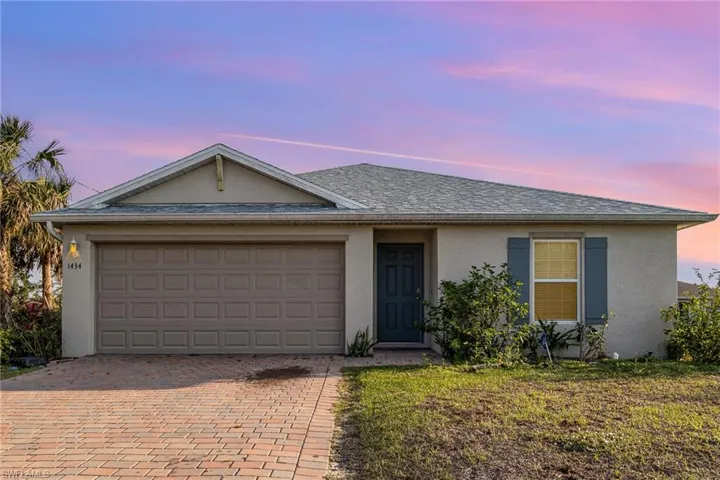 Ranch-style house with an attached garage, a shingled roof, decorative driveway, stucco siding, and a front yard