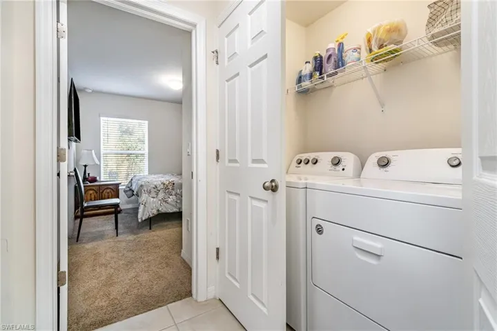 Washroom featuring light carpet, light tile patterned floors, and washing machine and clothes dryer