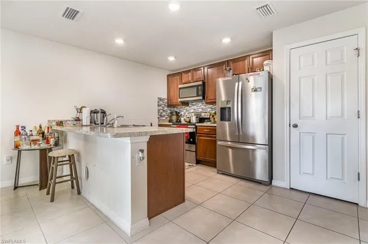 Kitchen with appliances with stainless steel finishes, brown cabinetry, visible vents, and tasteful backsplash