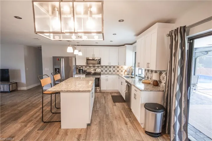 Kitchen with a breakfast bar, a center island, stainless steel appliances, light stone counters, and white cabinetry