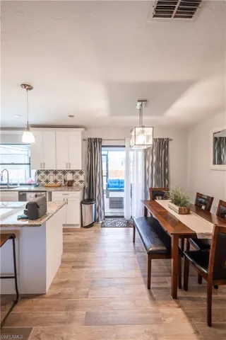 Kitchen with white cabinets, backsplash, light stone countertops, pendant lighting, and light wood finished floors