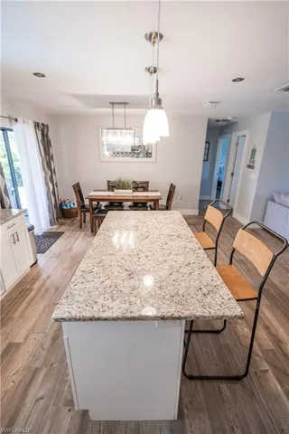 Kitchen featuring a kitchen breakfast bar, light stone countertops, a center island, decorative light fixtures, and light wood-style floors