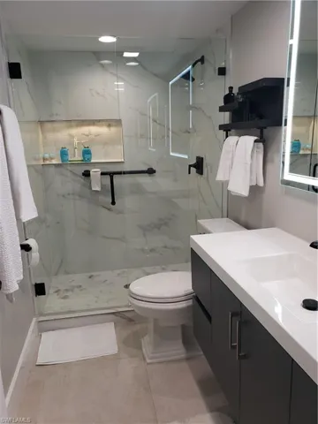 Bathroom features floating vanity with lighted mirror and large format tile on shower wall and custom glass and door