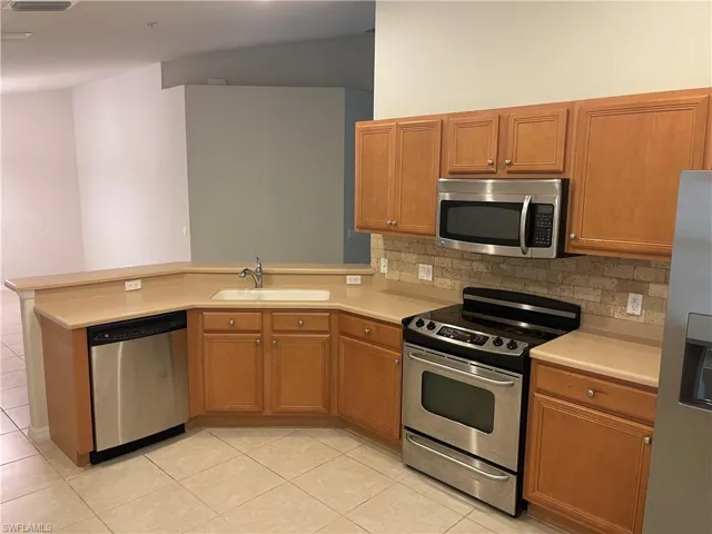 Kitchen featuring stainless steel appliances, a peninsula, light countertops, and wood finish cabinetry
