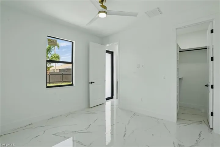 Unfurnished bedroom featuring baseboards, a spacious closet, ceiling fan, light marble finish floors, and a closet