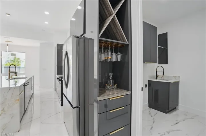 Bar featuring freestanding refrigerator, a sink, light marble finish flooring, recessed lighting, and baseboards