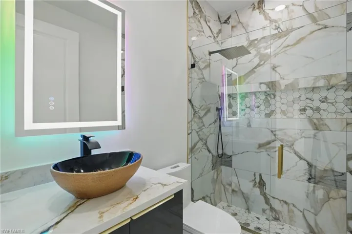 Bathroom with toilet, a marble finish shower, and vanity
