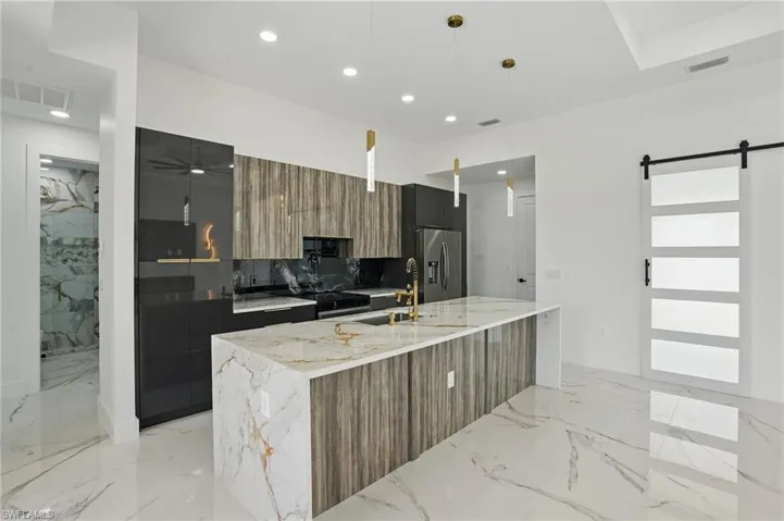 Kitchen featuring modern cabinets, stainless steel fridge, a sink, light marble finish flooring, and a barn door