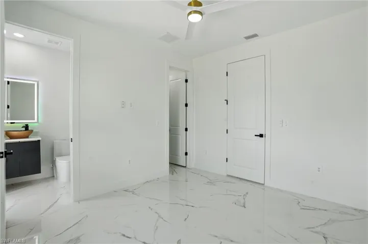 Unfurnished bedroom with baseboards, connected bathroom, light marble finish flooring, and a ceiling fan