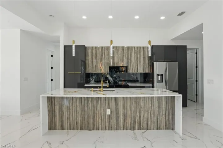 Kitchen featuring modern cabinets, stainless steel fridge, a spacious island, recessed lighting, and light marble finish floors