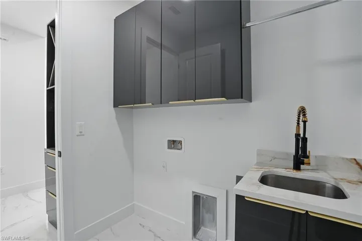 Washroom with cabinet space, washer hookup, light marble finish flooring, and baseboards