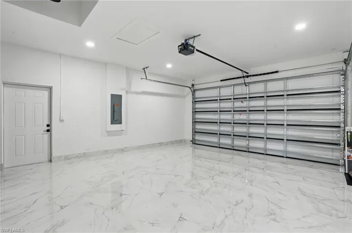 Garage with a garage door opener, electric panel, and recessed lighting