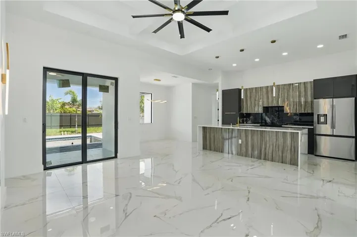 Kitchen featuring stainless steel refrigerator with ice dispenser, modern cabinets, recessed lighting, a ceiling fan, and a kitchen island with sink