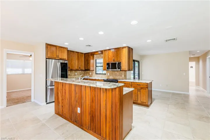 Kitchen with stainless steel appliances, light stone counters, tasteful backsplash, and a center island with sink