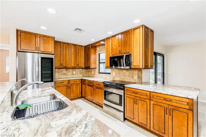 Kitchen featuring decorative backsplash, stainless steel appliances, light stone counters, and sink