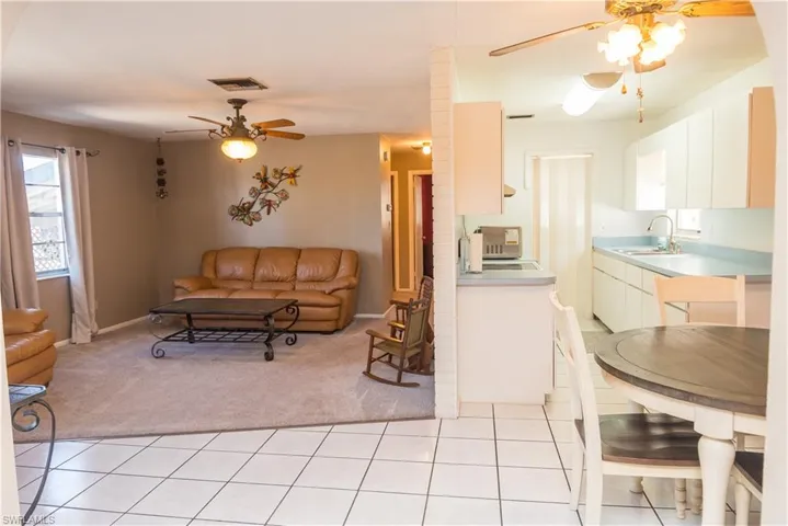 Living room with a ceiling fan, light tile patterned floors, and light colored carpet