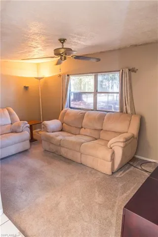 Carpeted living room with ceiling fan and a textured ceiling