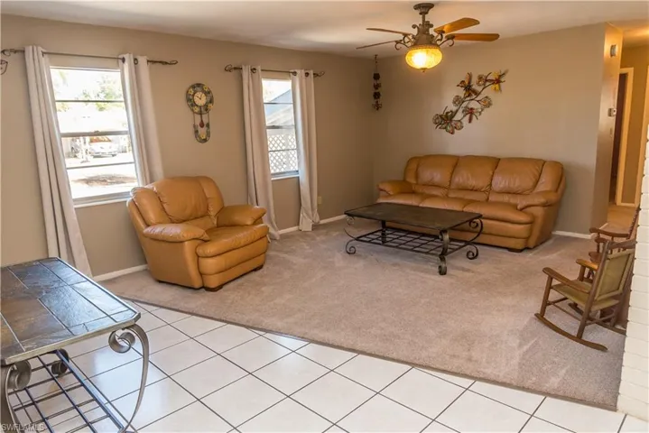 Living room with ceiling fan, light carpet, and light tile patterned flooring