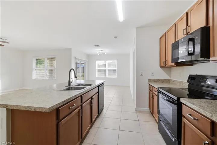 Kitchen featuring wood cabinetry, stone-finish countertops, and black appliances