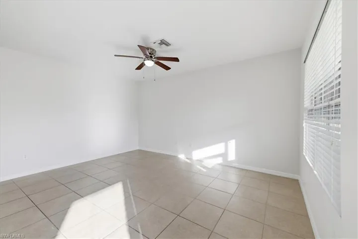 Neutral-toned ceramic tile flooring, white walls, window with horizontal blinds, and a ceiling fan with integrated lighting