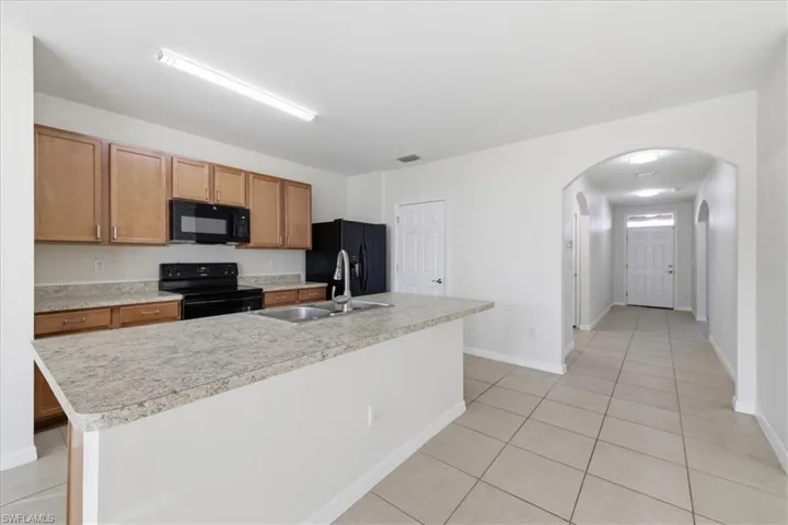 Kitchen featuring wood-finish cabinetry, light-toned countertops, black appliances, and a stainless steel sink