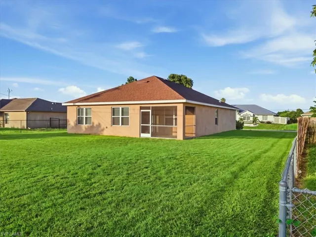 Expansive rear lawn with perimeter chain-link fencing, stucco exterior, and a screened-in patio